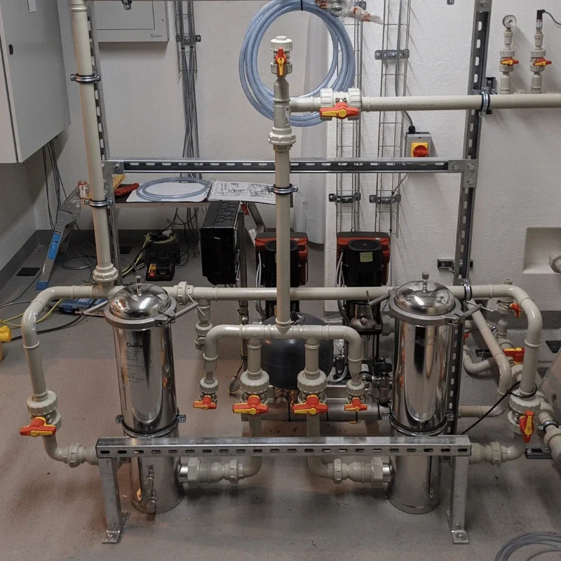 Bespoke containerised water treatment plant built in Northampton, featuring stainless steel filter housings, pressure vessel, red-handled ball valves, duty/standby circulation pumps, and grey UPVC pipework manifold, designed for a large-scale data centre cooling and process water application.